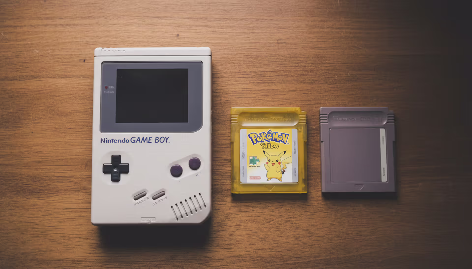 Original Nintendo Game Boy console in classic gray color lying on a table next to Tetris and Pokemon game cartridges, top-down view with soft natural lighting