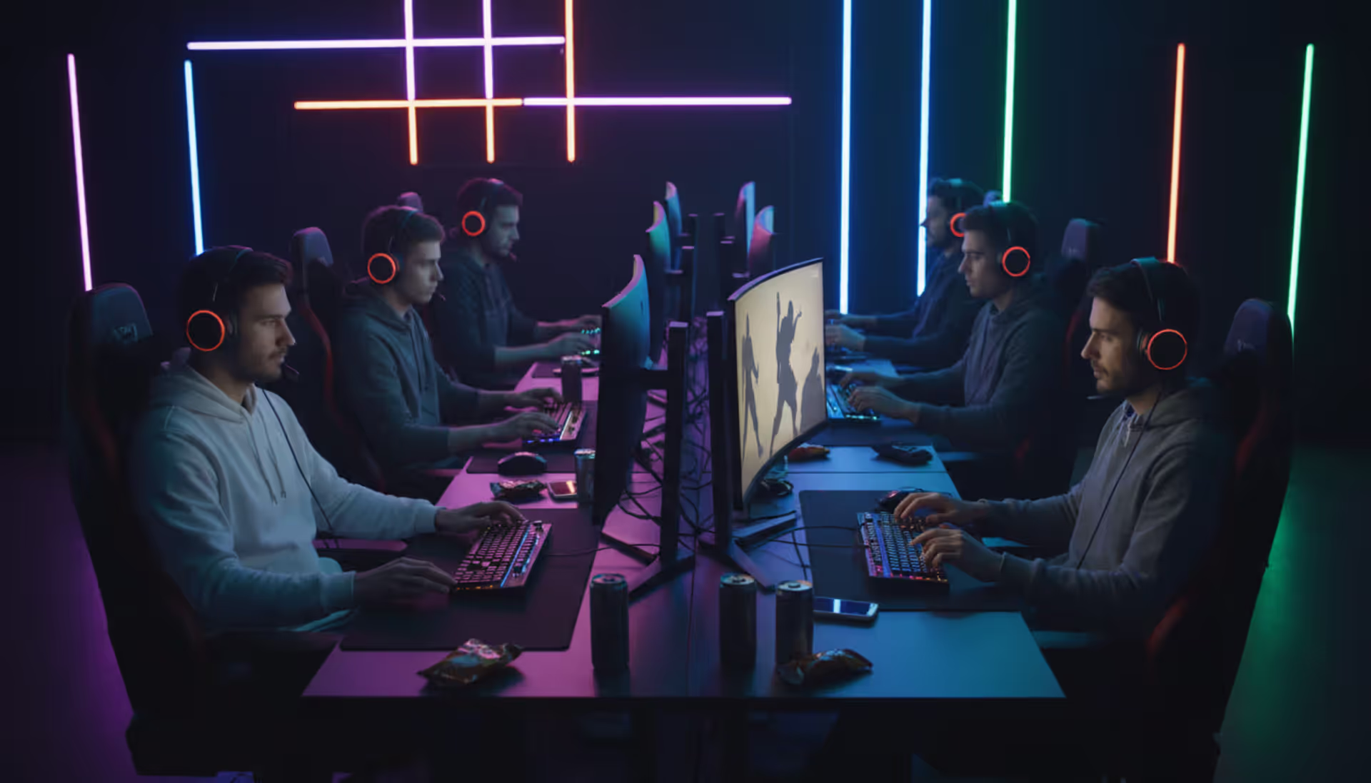 A group of gamers wearing headsets playing multiplayer games on large monitors with neon RGB lighting in a dark room
